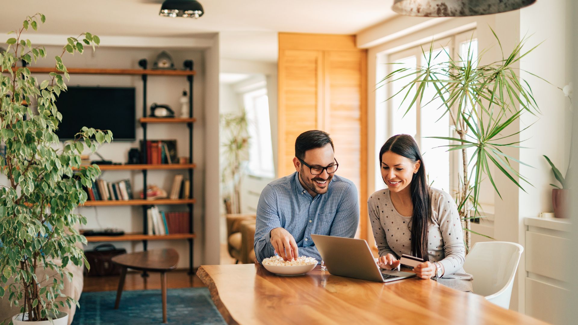 Two people smiling and working together at home with laptop and popcorn