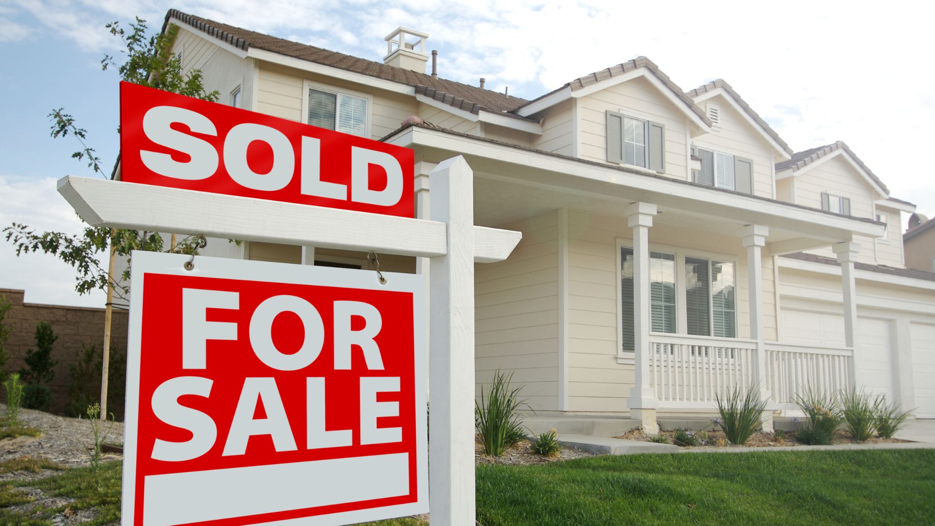 Red sold sign in front of a white two-story suburban house