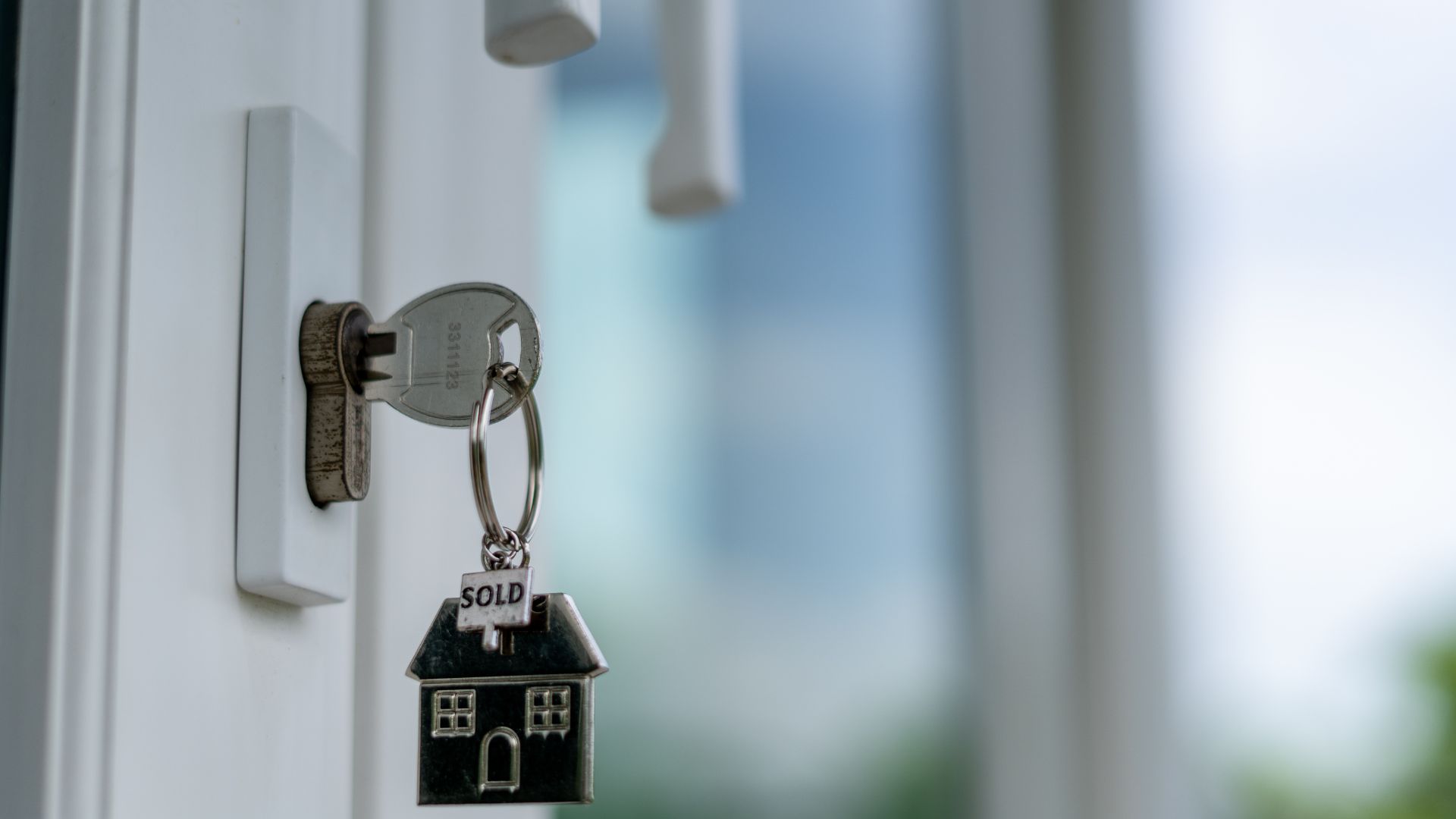 House key with "SOLD" keychain hanging in door lock