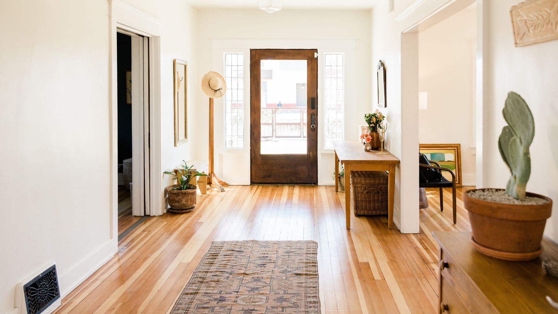 Bright entryway with wooden floor, plants, straw hat, and glass door