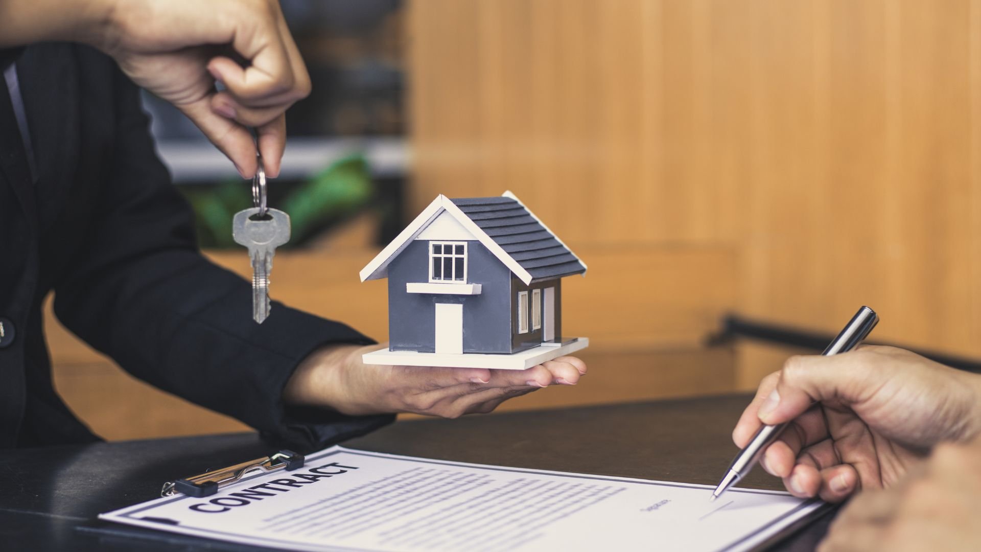 Hand holding house keys and model home over real estate contract